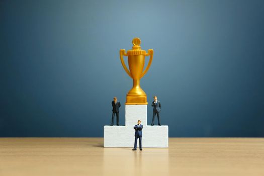 Miniature business concept - businessman standing in front of white winner podium with golden trophy. Image photo