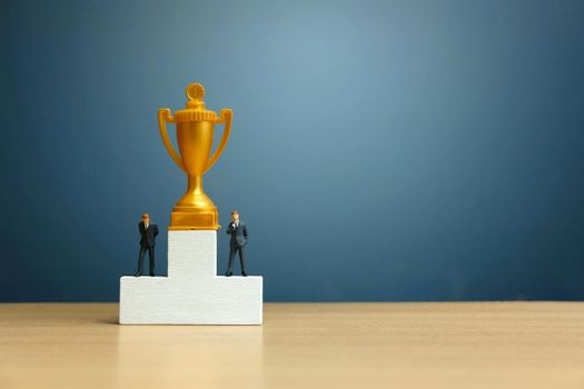 Miniature business concept - businessman standing in front of white winner podium with golden trophy. Image photo