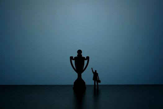 Business strategy conceptual photo - Silhouette of miniature businessman pointing on winning trophy. Image photo