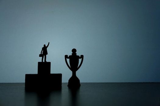 Business strategy conceptual photo - Silhouette of miniature businessman standing on podium pointing on trophy. Image photo