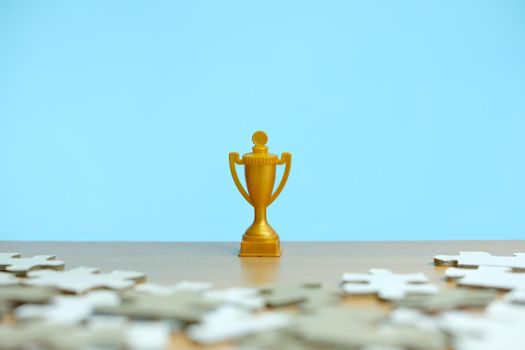 a golden trophy stands between a pile of puzzles. Image photo