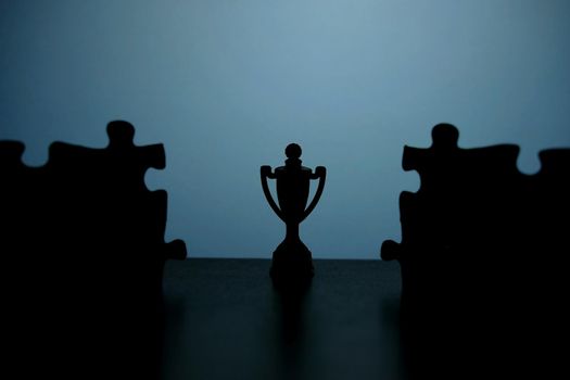 Business strategy conceptual photo – Silhouette of trophy stand in the middle of jigsaw puzzle. Image photo