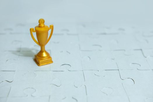 a golden trophy stands between a pile of puzzles. Image photo