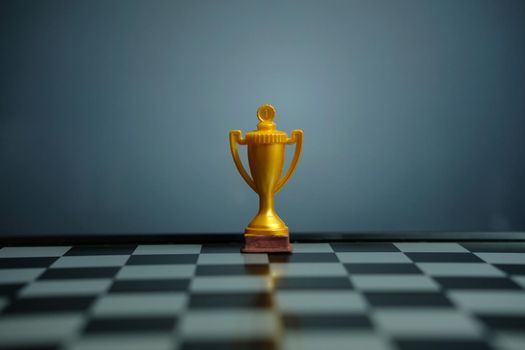 Business strategy conceptual photo – Golden trophy standing on chessboard with chess pawn. Image photo