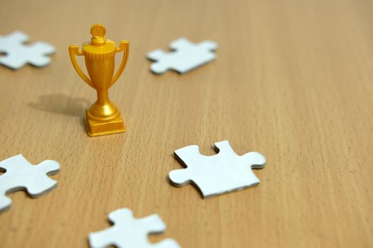 a golden trophy stands between five option/alternative jigsaw puzzles. Image photo