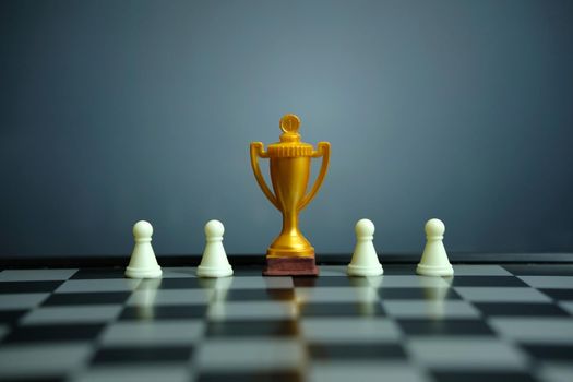 Business strategy conceptual photo – Golden trophy standing on chessboard with chess pawn. Image photo