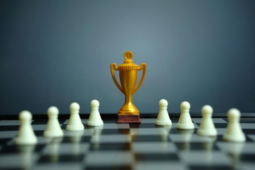 Business strategy conceptual photo – Golden trophy standing on chessboard with chess pawn. Image photo