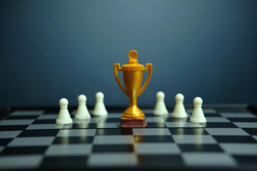 Business strategy conceptual photo – Golden trophy standing on chessboard with chess pawn. Image photo