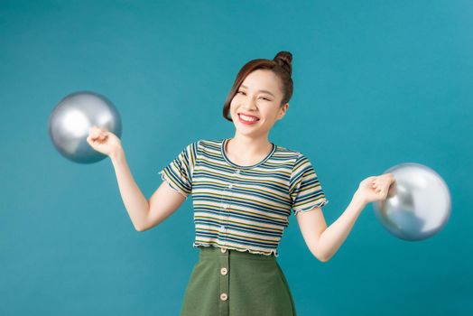 Young happy woman holding silver balloons on blue background