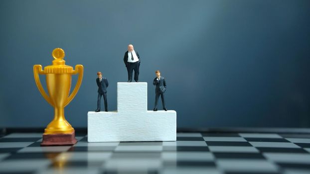 Miniature business concept - businessman standing on white winner podium with golden and silver trophy. Image photo
