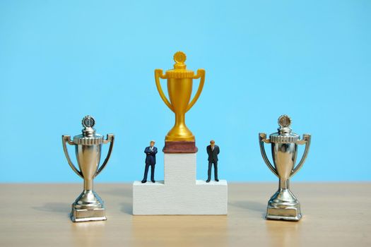 Miniature business concept - businessman standing on white winner podium with golden and silver trophy. Image photo