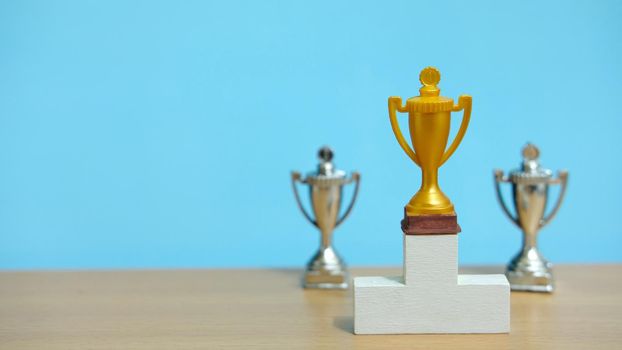 Golden trophy standing on white podium with two silver trophy at back. Image photo