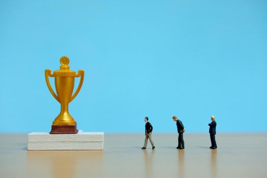 Miniature business concept - group of businessman lining up behind the golden trophy. Image photo