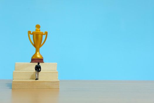 Miniature business concept - businessman walking on staircase to reach golden trophy. Image photo