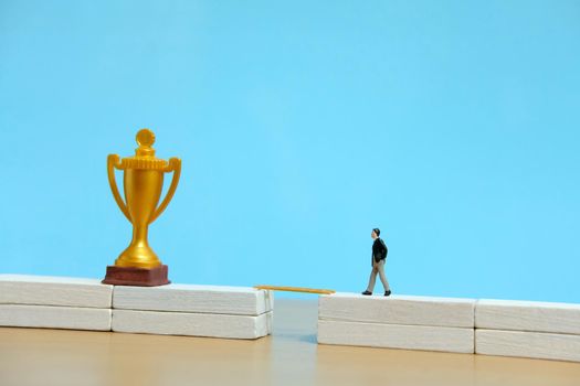 Miniature business concept - businessman walking toward golden trophy above white bridge. Image photo