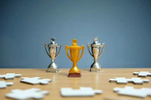 Gold and silver trophy stands between infront of jigsaw puzzles. Image photo