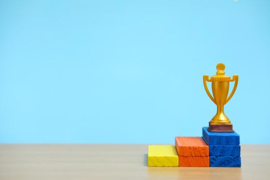 Golden trophy standing at colorful podium on wooden table. Image photo