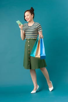 Smiling young Asian woman with shopping colour bags over blue background.