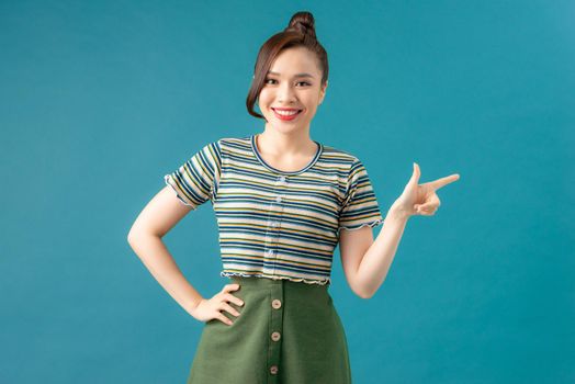 Young asian cute woman isolated on blue background smiling cheerfully pointing with forefinger away.