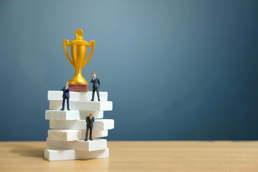 Miniature business concept - businessman standing on white staircase ladder with golden trophy above it. Image photo