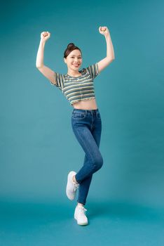 Full length portrait of a joyful young woman jumping and celebrating over  blue background