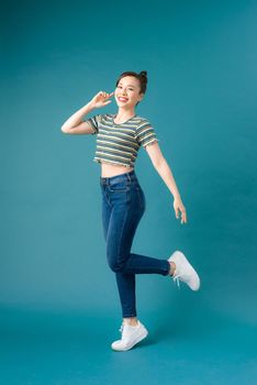 Full length portrait of a cheerful casual asian woman jumping isolated over blue background