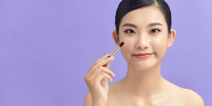 Closeup shot of beautiful woman applying eyeshadow on eyelid using makeup brush