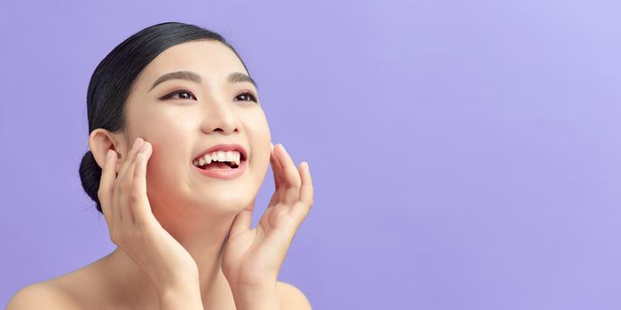 Beautiful smiling asian girl model with natural makeup touching glowing hydrated skin