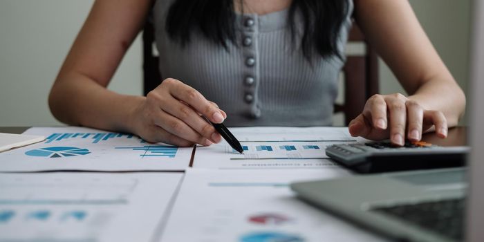 Business woman working in finance and accounting Analyze financial budget with calculator and laptop computer at home.