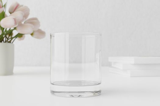 Empty water glass mockup on table with tulips and books.