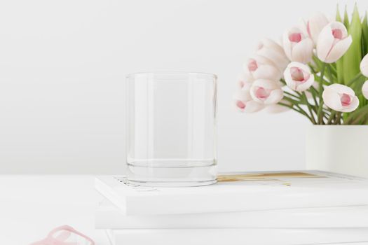 Empty water glass mockup on table with tulips and books.