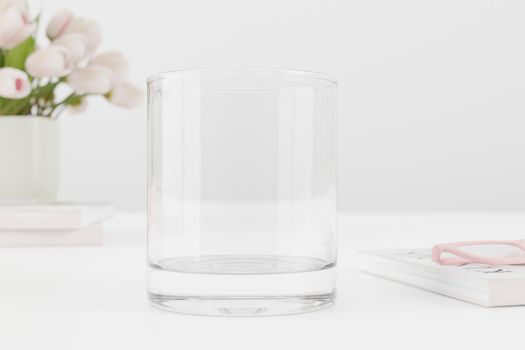 Empty water glass mockup on table with tulips and books.
