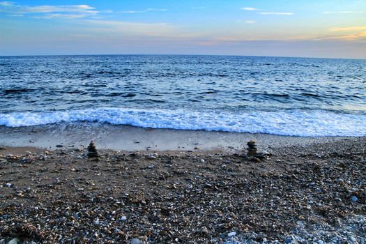 Round stacked stones on the Isla Plana beach at sunset in Cartagena. Waves in the background.