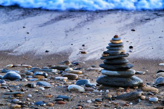 Round stacked stones on the Isla Plana beach at sunset in Cartagena. Waves in the background.