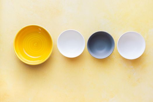 Assorted ceramic multicolored empty bowls on rustic yellow surface. Top view, blank space
