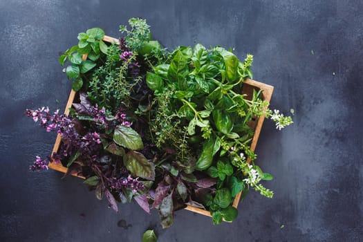 Fresh herbs ingredients for healthy cooking or salad making in a wooden crate.  Rustic dark background, top view, blank space