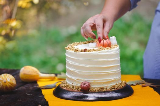 Woman decorating a pumpkin pie layer cake  at a garden party. Unrecognizable woman decorating cake with pumpkins.  Selective focus, copy space