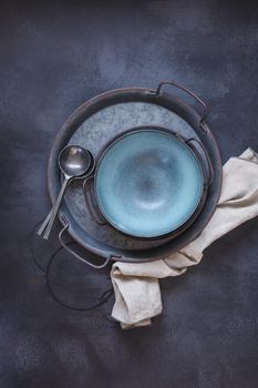 Empty blue ceramic bowl with vintage cutlery  on rustic metal tray. Top view, blank space