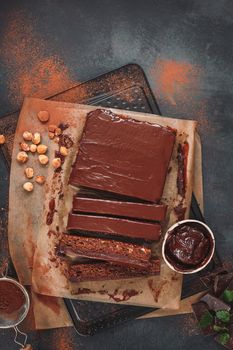 Chocolate slices with hazelnuts and seeds. Messy, dark moody setting. Top view, blank space