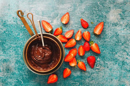 Saucepan of melted chocolate and strawberry pieces  beside. Top view, blank space