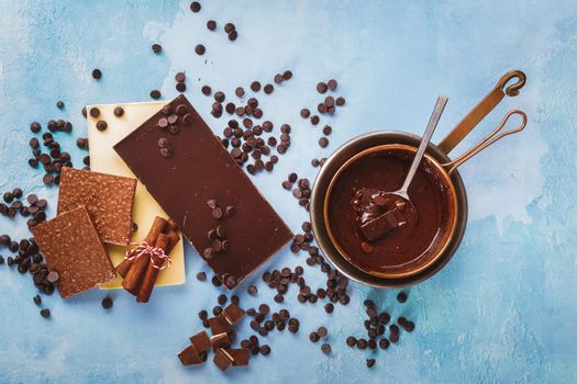 Melted chocolate in copper pan and  bars of dark and white chocolate beside on rustic blue surface. Top view, blank space