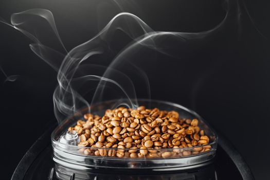 fresh roasted coffee beans with smoke in coffeemaker bean container, close-up view