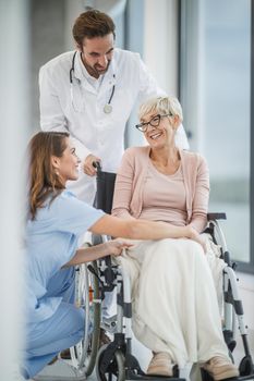 Successful doctor and young nurse talking with their senior female wheelchair-bound patient.