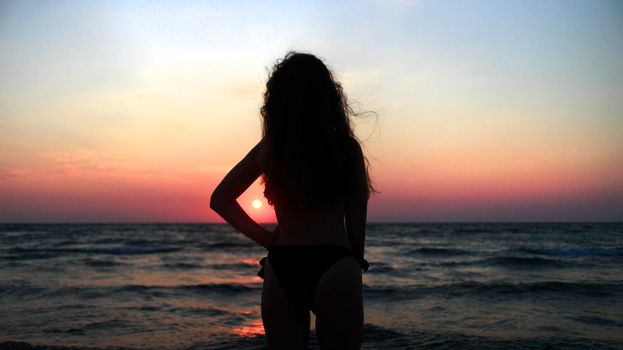 A curly girl standing in front of a sunset. Woman silhouette. At the sea