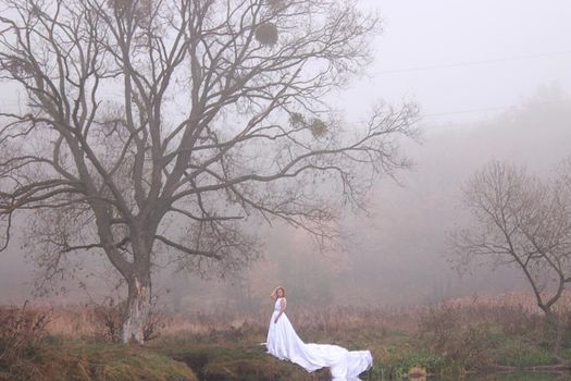 A redhead women in a white dress. A bride. in the forest near the lake