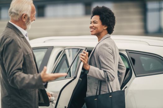 A senior chauffeur opening a car door for black business woman before their business trip.