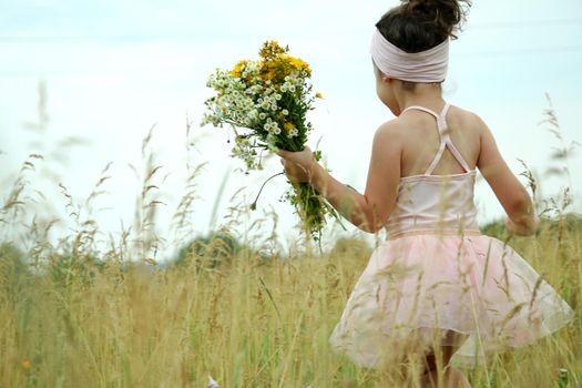 Little girl with flowers in pink dress playing in the field happy