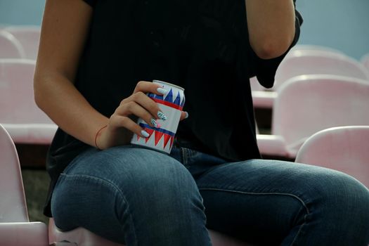 A women in black t-shirt sitting on a chair holding a metal can with a drink