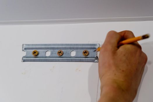 Worker marks the place for fixing the dowels with a pencil. Close up.