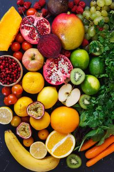 Assortment of different fruits and vegetables in rainbow colors on dark rustic surface,  Healthy eating background